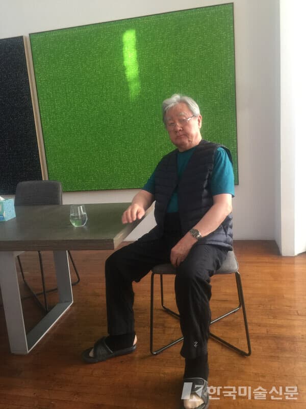 마에자와 유사쿠가 구입 소장하고 있는 &lsquo;WATER YLWG&rsquo;(17 / 66&times;82 inches) 작품 앞에 앉아 있는 안영일 작가