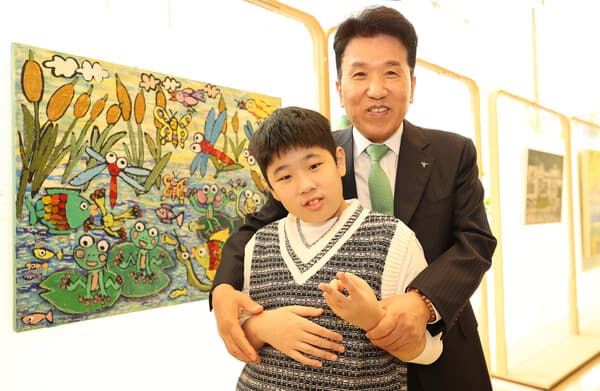 하나금융그룹은 '제45회 장애인의 날'을 기념해 4월 17일 하나은행 본점에서 발달장애 예술가들과 함께하는 미술 공모전 '제4회 하나 아트버스(Hana Artverse)' 시상식을 개최했다. 함영주 하나금융그룹 회장(사진 오른쪽)이 이날 아동&middot;청소년부문 우수상 수상작인 이도원 작가의 '연못마을 개구리와 친구들' 작품 앞에서 이도원 작가와 함께 기념 촬영을 하고 있다. [사진=하나금융그룹]